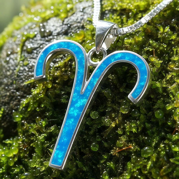 Close-up of the Aries ram glyph pendant inlaid with blue opal in a sterling silver setting, resting on moss