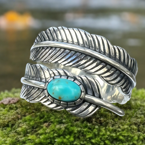 Close-up of the sterling silver feather ring with an oval blue howlite stone, resting on moss