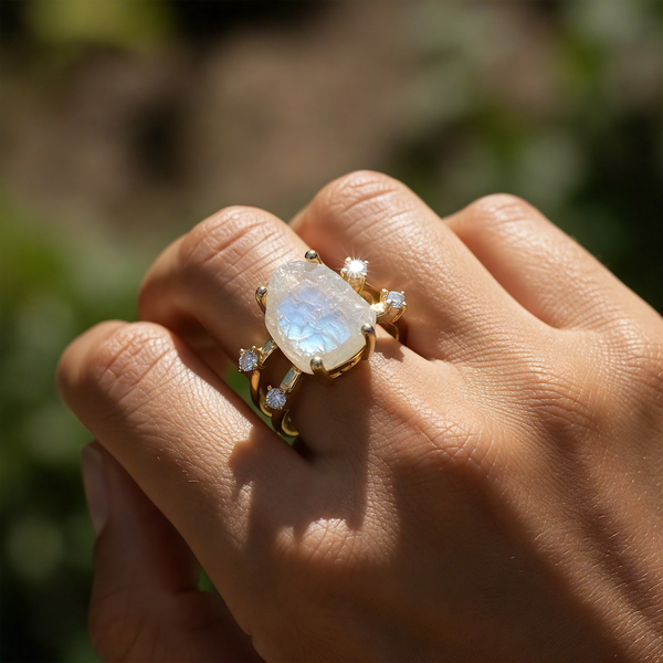 The moonstone and gold ring worn on a hand in warm sunlight