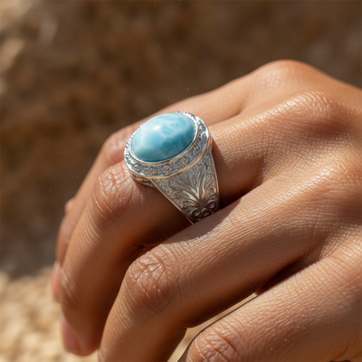 The larimar ring worn on a hand in warm sunlight, showing the oval stone and the engraved silver shoulder