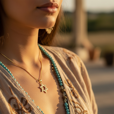 The gold Star of David pendant worn at the collarbone in warm sunlight, styled with a beaded necklace