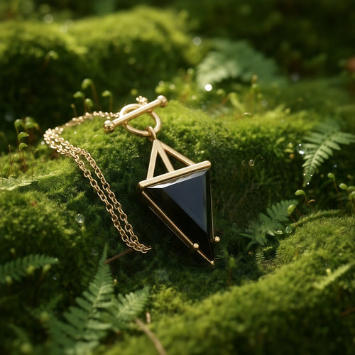 Black onyx triangle pendant in a gold frame on a gold cable chain, resting on moss