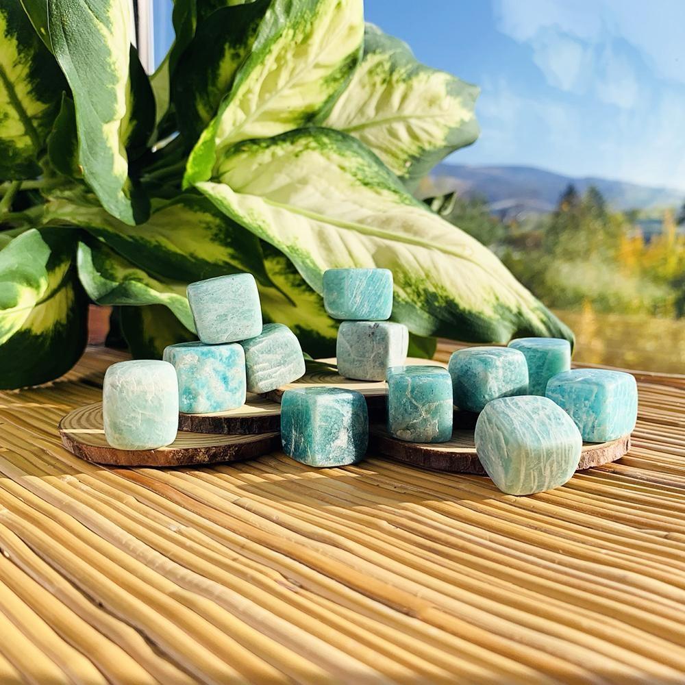 Aqua-green amazonite tumbled cubes with white streaks stacked on wood slices beside a leafy plant