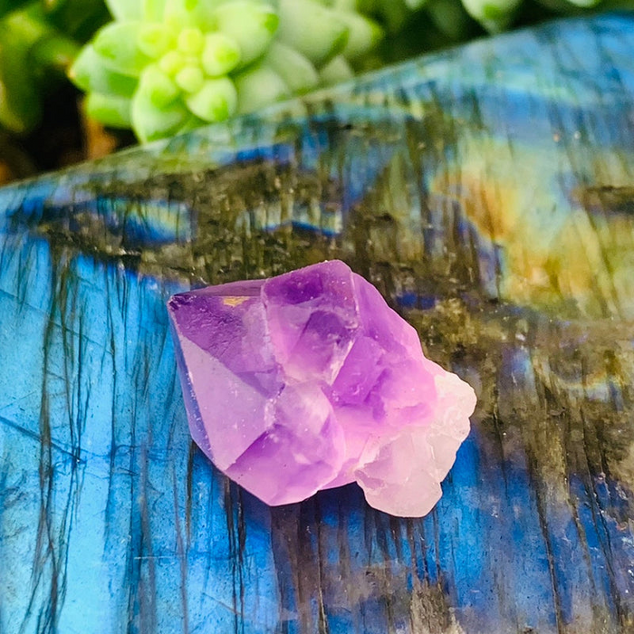 A pale purple fairy amethyst cluster on a labradorite slab