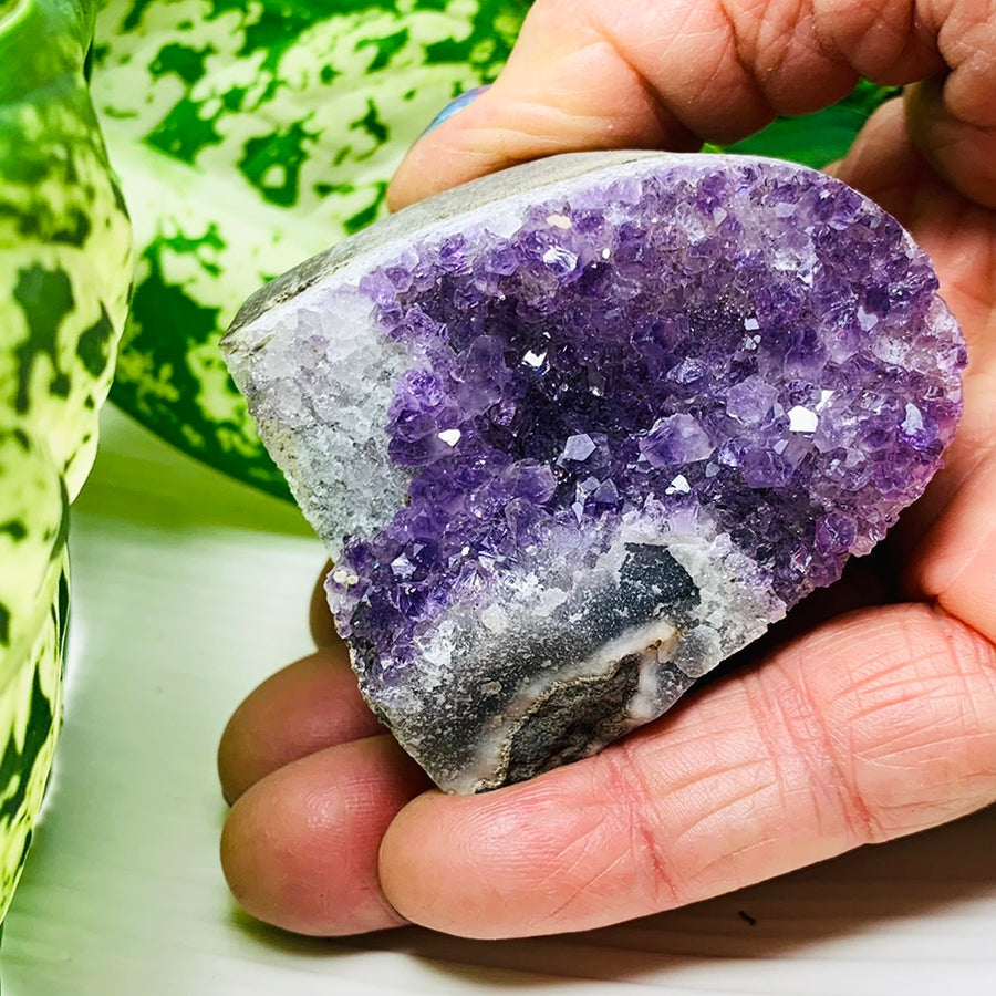 An amethyst geode freeform resting in an open hand, its purple crystals filling most of the palm