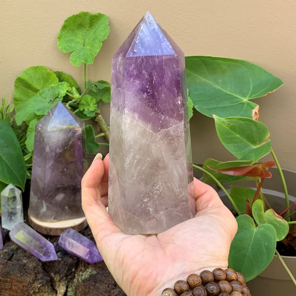 A tall amethyst tower standing upright on an open palm, purple at the tip and clear toward the base