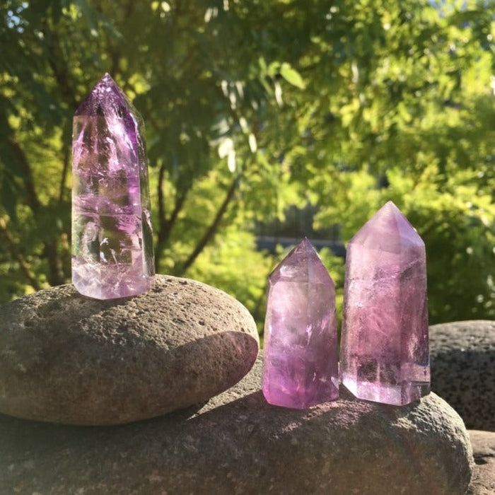 Three amethyst points of different shades standing on river stones in the sun