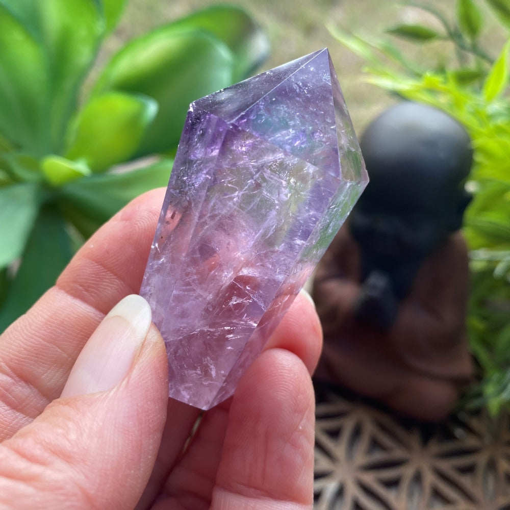 Faceted amethyst wand with a six-facet point held between two fingers