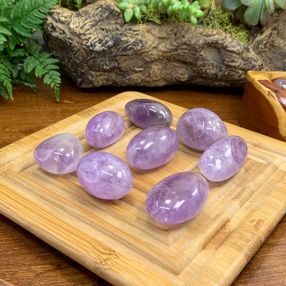 Eight polished amethyst tumbled stones on a bamboo board, from pale lilac to deeper violet