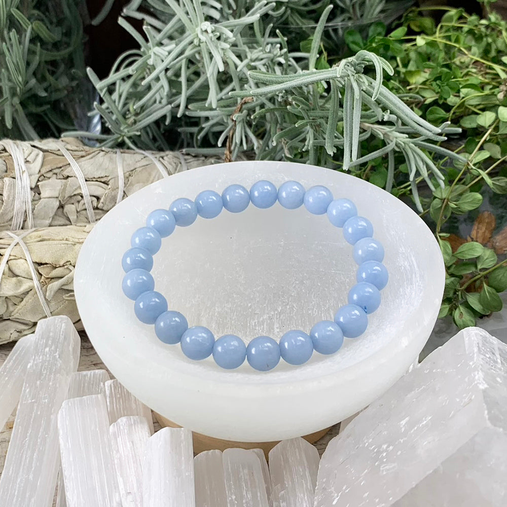 Angelite mala bracelet of round pale blue beads resting in a selenite bowl