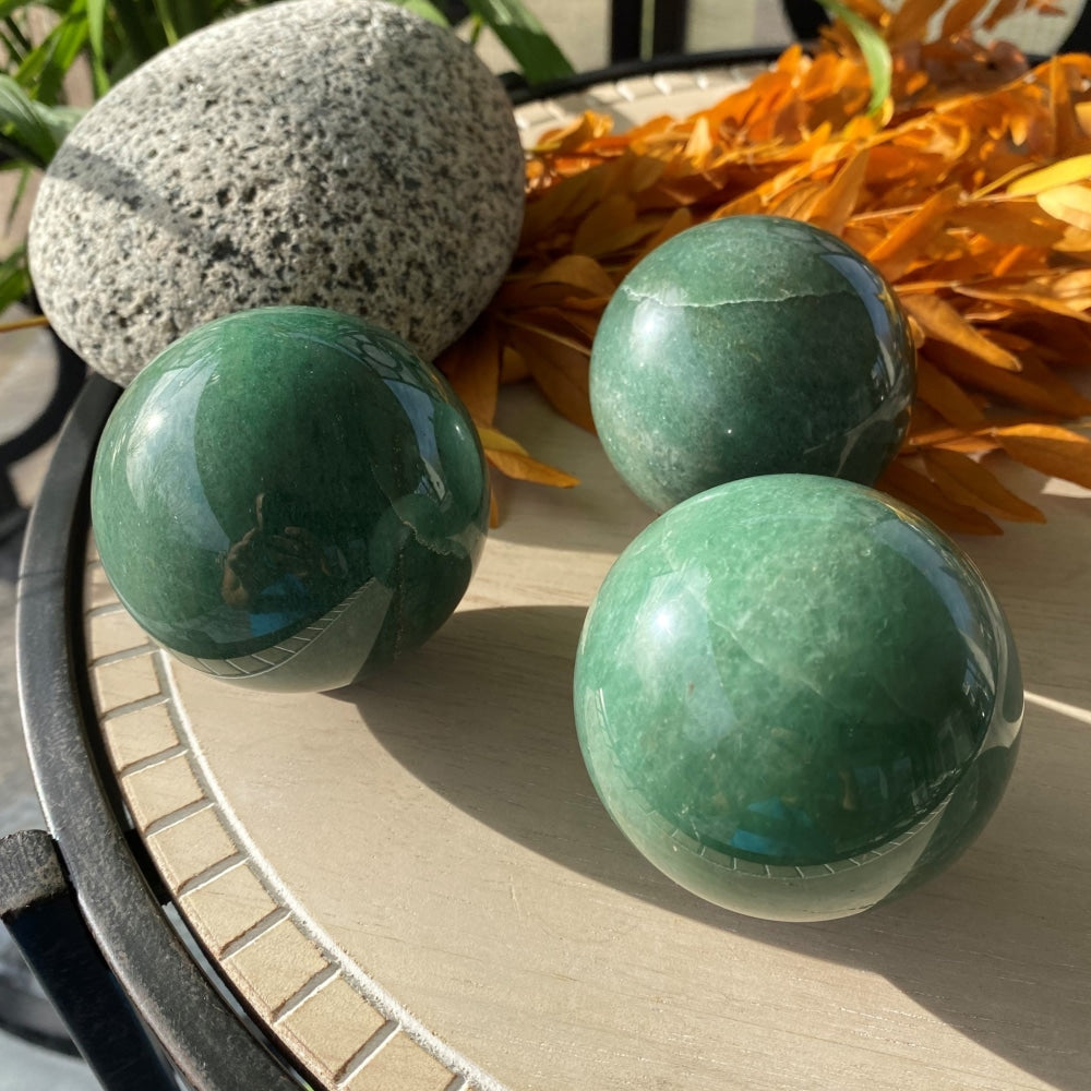 Three polished green aventurine spheres on a sunlit table, each with its own veins and shade of green
