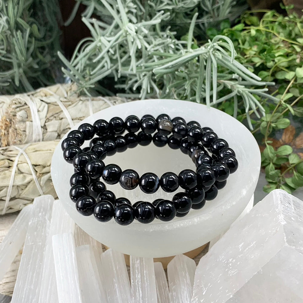 Black agate mala bracelets of round 8 mm beads resting in a selenite bowl