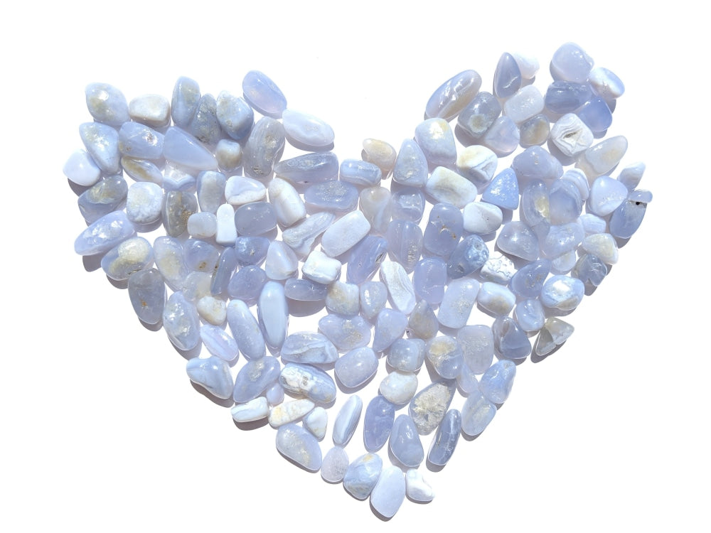 Dozens of tumbled blue lace agate stones arranged in a heart, in shades from pale lilac-blue to milky white
