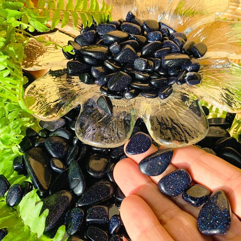 A few sparkling deep blue tumbled sandstone pieces resting on fingers beside a glass dish piled with more