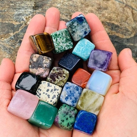 Two cupped hands holding nineteen colourful tumbled crystal cubes