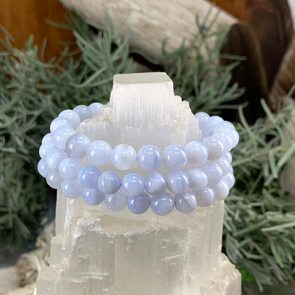 Close-up of blue lace agate bead bracelets stacked on a selenite tower, showing the pale blue banding of each bead