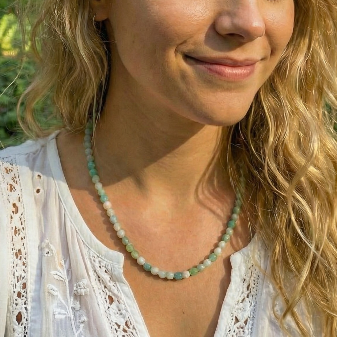 A smiling woman in a white lace blouse wearing the Caribbean jasper bead necklace at her collarbone