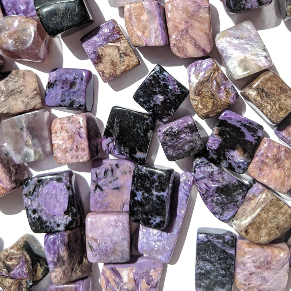 Many charoite tumbled stones in lilac, violet, deep purple, black, white and brown