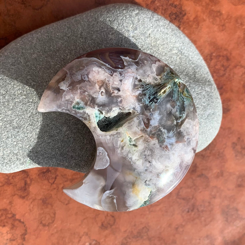 Close-up of a polished cherry flower agate crescent moon with white blossom-like inclusions, leaning on a smooth gray stone