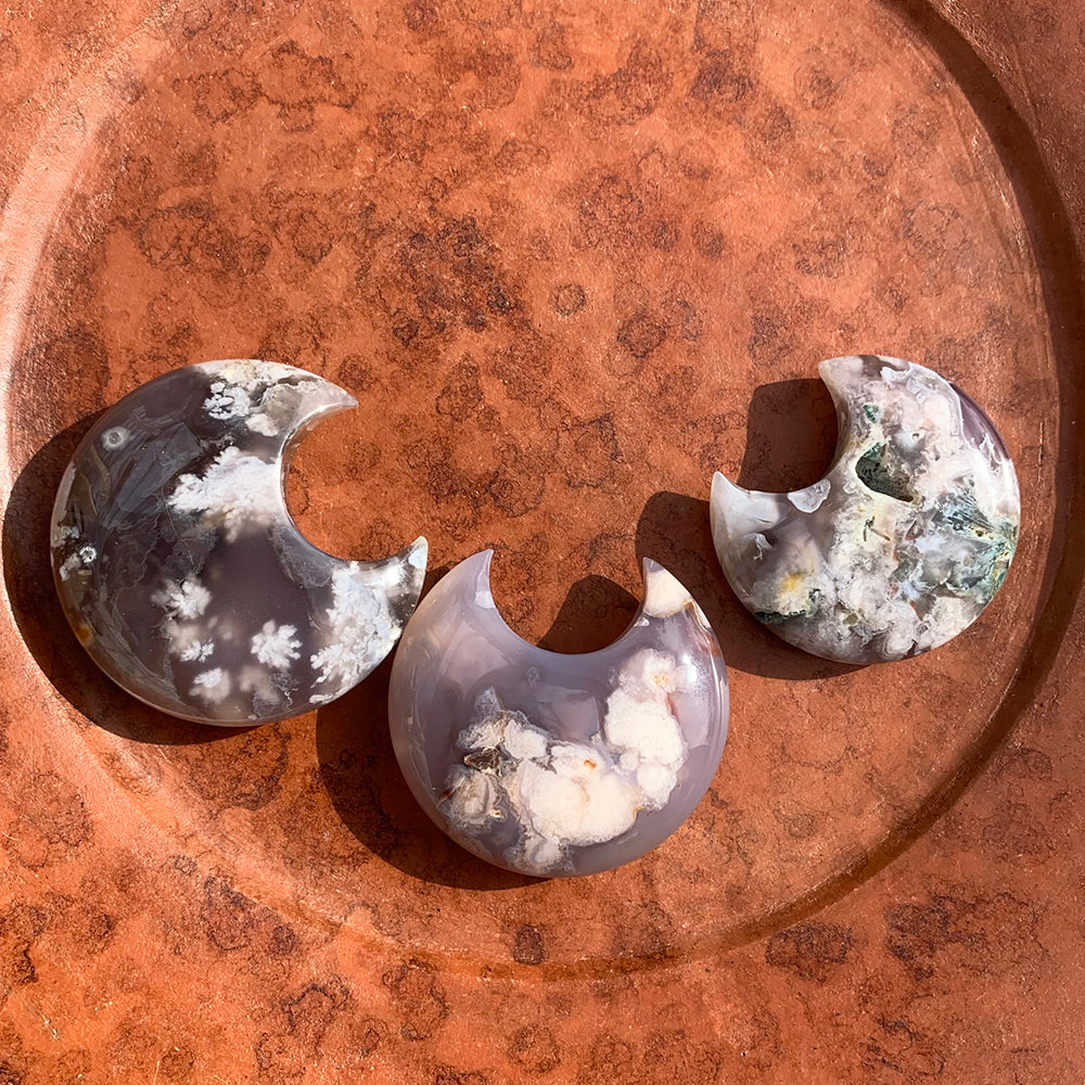 Three cherry flower agate crescent moons on a burl wood dish, each with its own pattern of white blossoms and gray-lavender agate