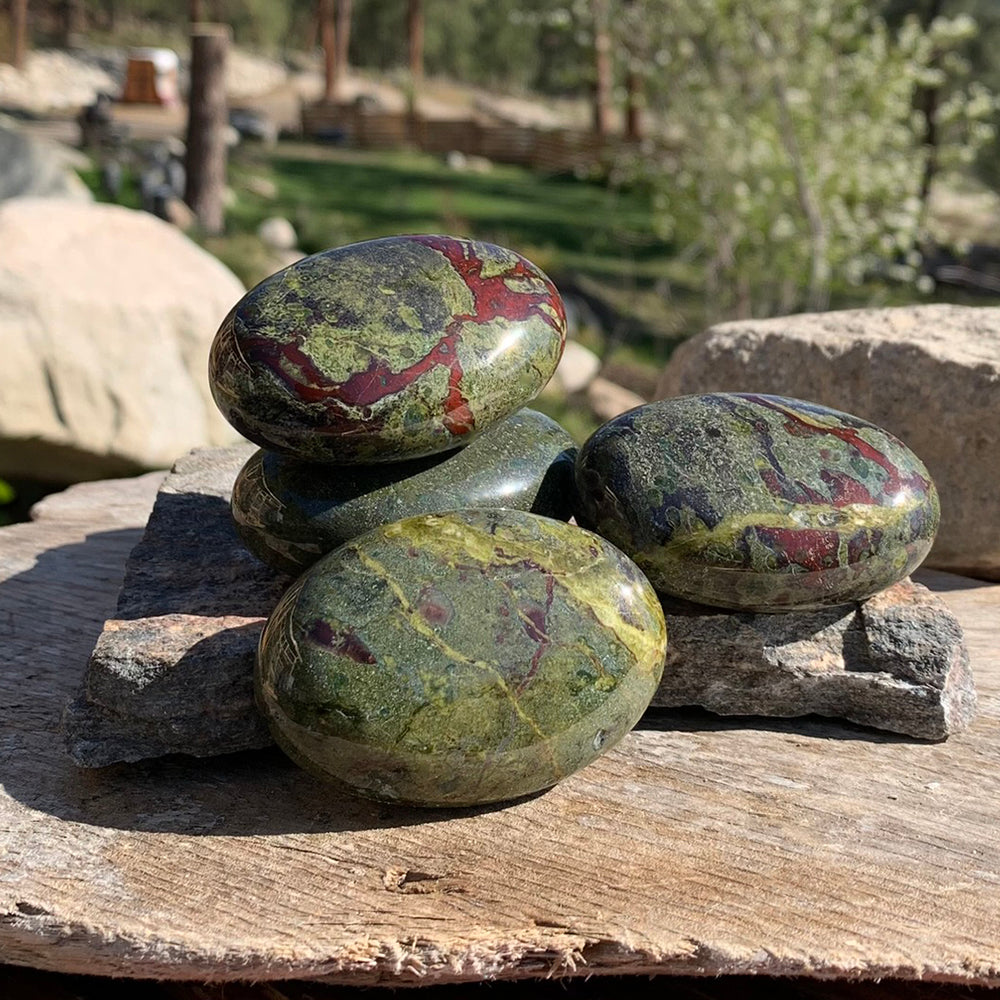 Four dragon blood jasper palmstones in sunlight on a flat rock, each with a different pattern of green and red