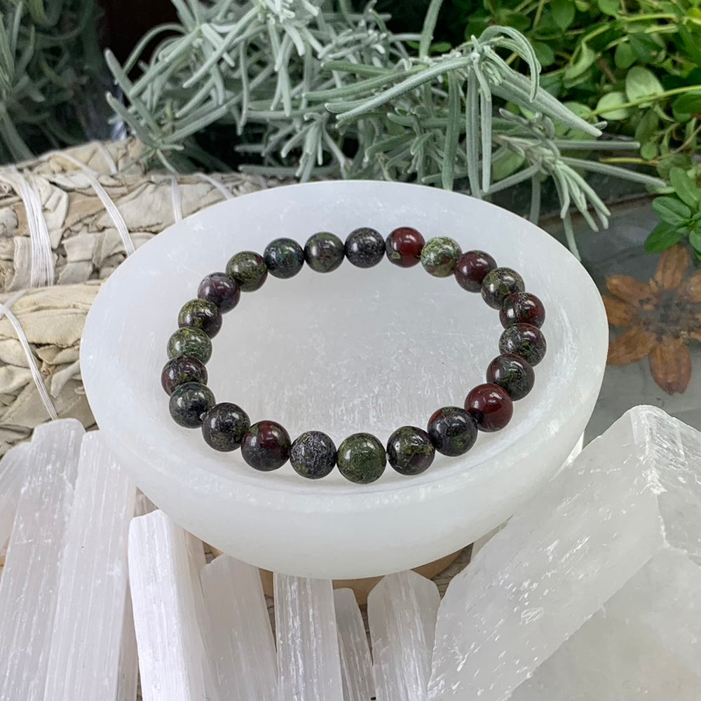 A single dragon&rsquo;s blood mala bracelet of round dark green and deep red beads resting in a selenite bowl