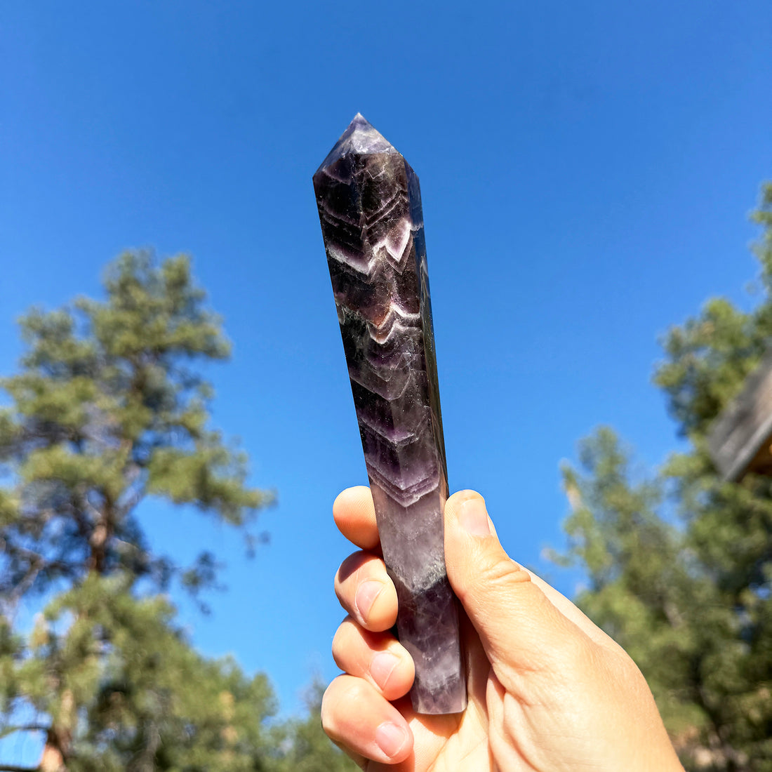 A hand holding the dream amethyst generator up to a blue sky, its deep purple body striped with white V-shaped chevron bands