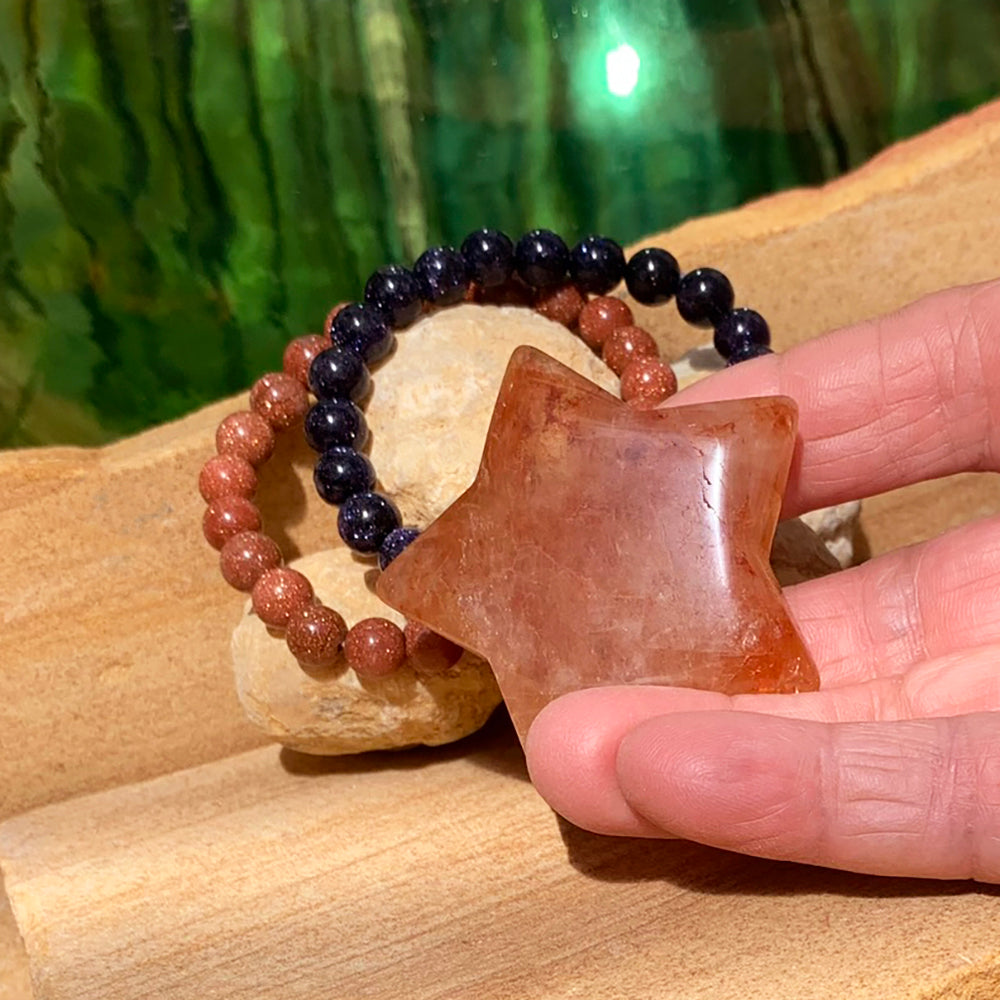 The fire quartz star resting on fingertips in front of the red and blue sandstone bracelets