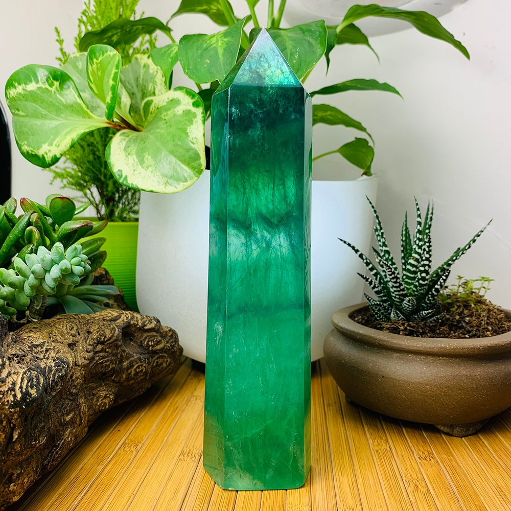 Green fluorite generator standing upright on a bamboo mat among potted plants, glowing deep green