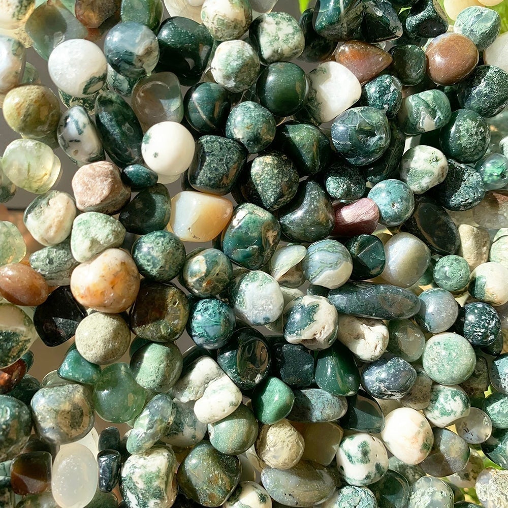 Close view of many tumbled moss agate stones in deep green, white, clear, brown and red, each with mossy inclusions