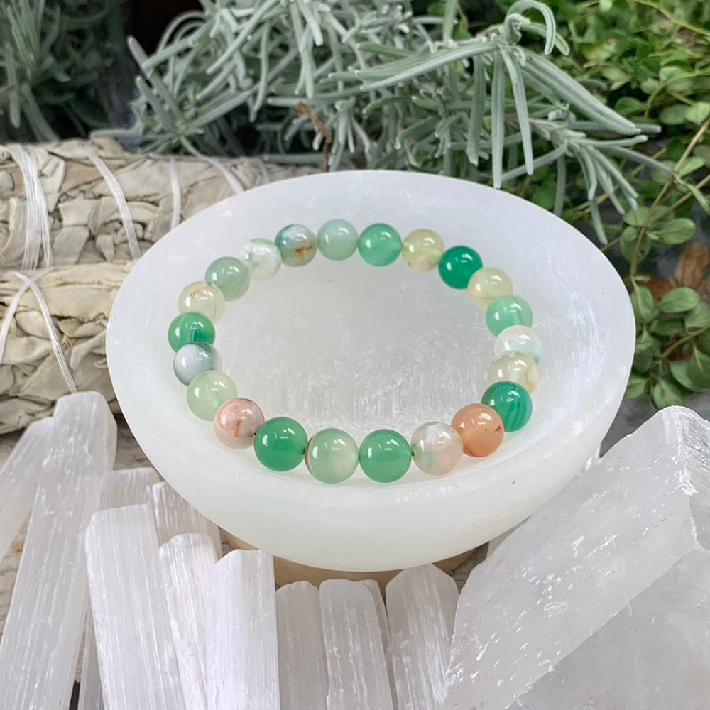 A green cherry agate bead bracelet in jade, mint, cream and peach tones resting in a selenite bowl