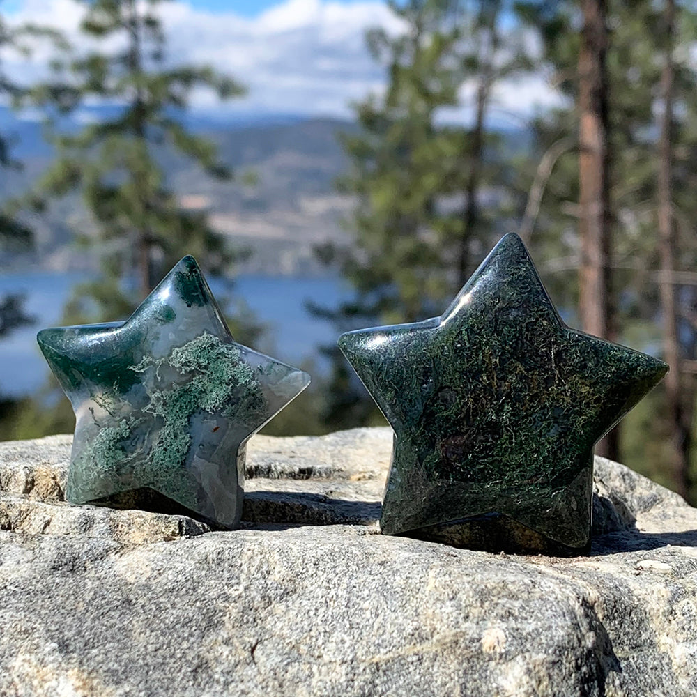 Two moss agate stars on a rock above a forest lake, one misty white with green moss patches, one deep forest green