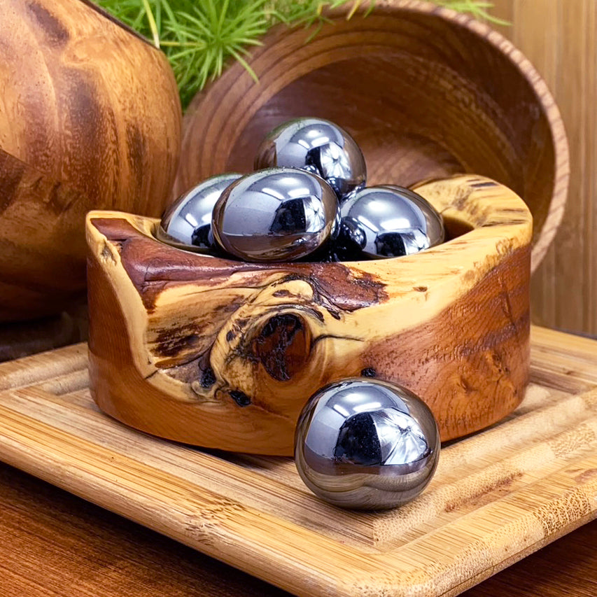 Glossy metallic hematite ellipses heaped in a wooden bowl, with one more resting on a bamboo board in front