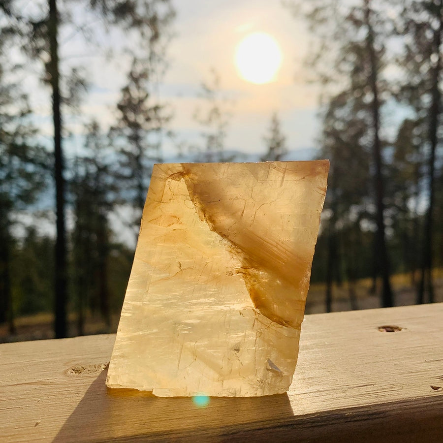 A honey calcite chunk on a wooden rail, glowing amber with the low sun shining behind it