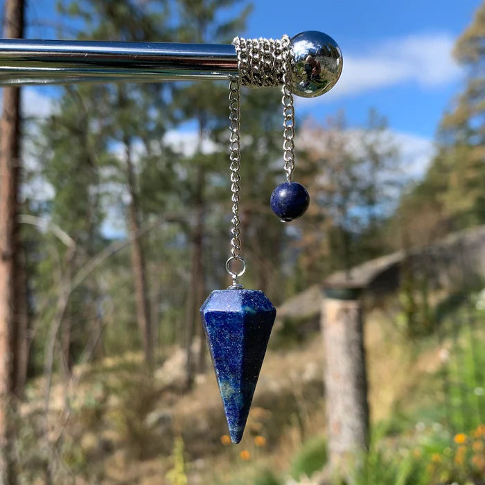 A faceted lapis lazuli pendulum hanging from its silver chain, with a lapis bead at the other end