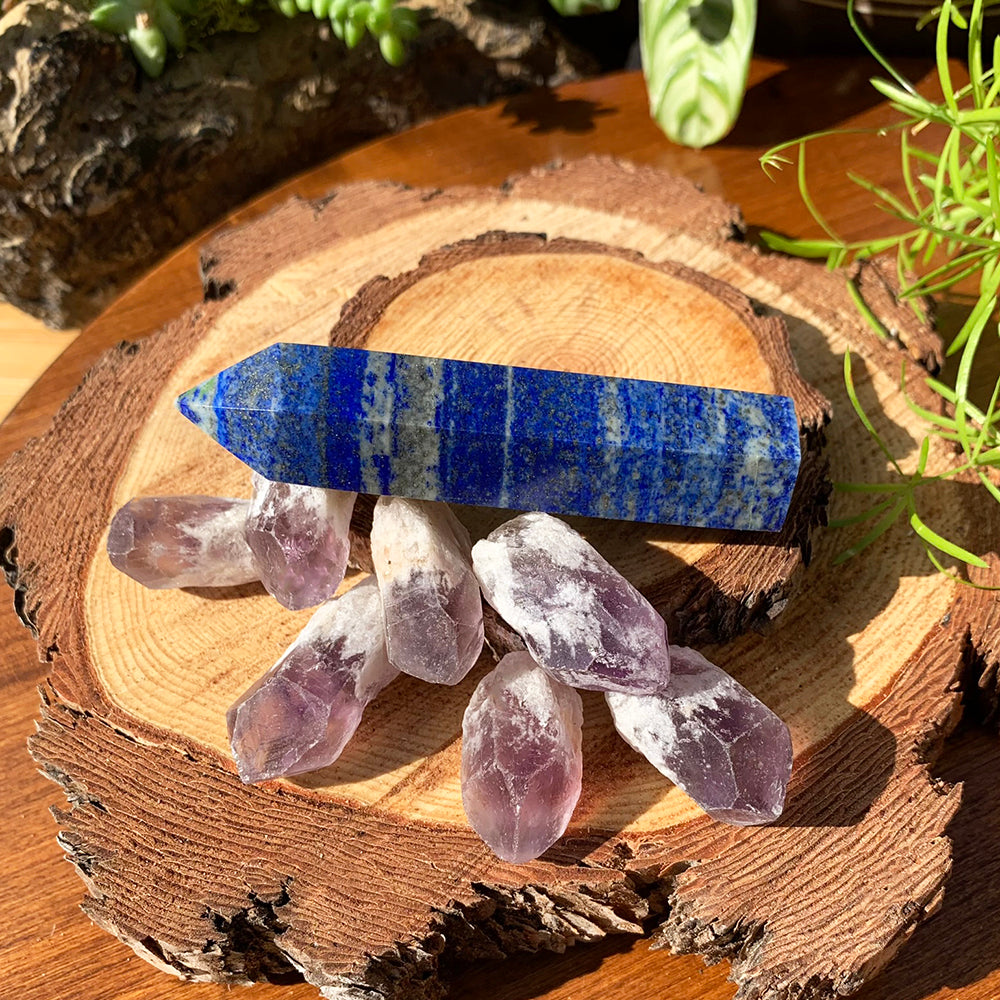 The full set on a wood slice: a deep blue lapis lazuli point lying above seven pale violet amethyst shards