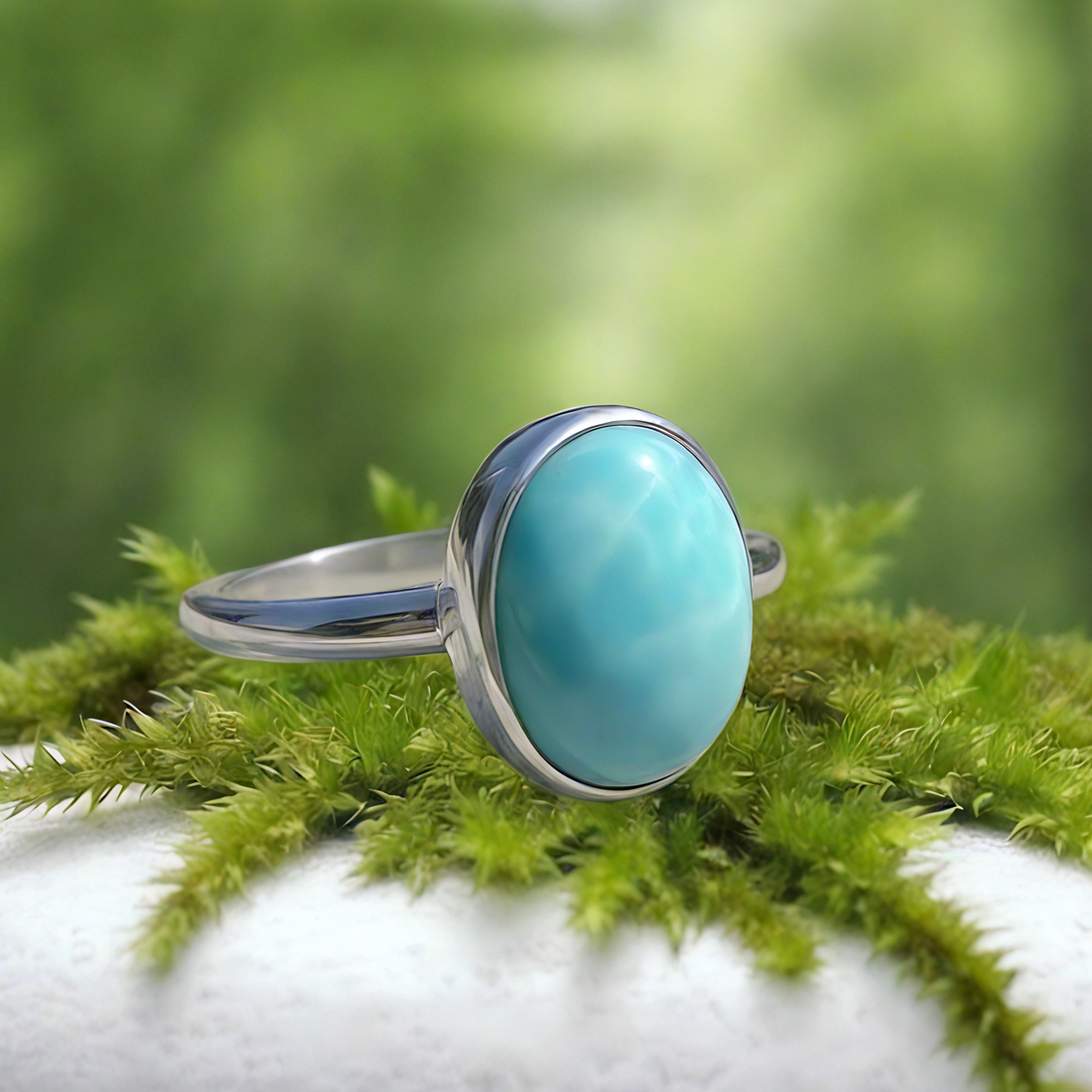 Larimar ring resting on green moss: a smooth oval sky-blue larimar stone in a polished silver bezel on a slim silver band