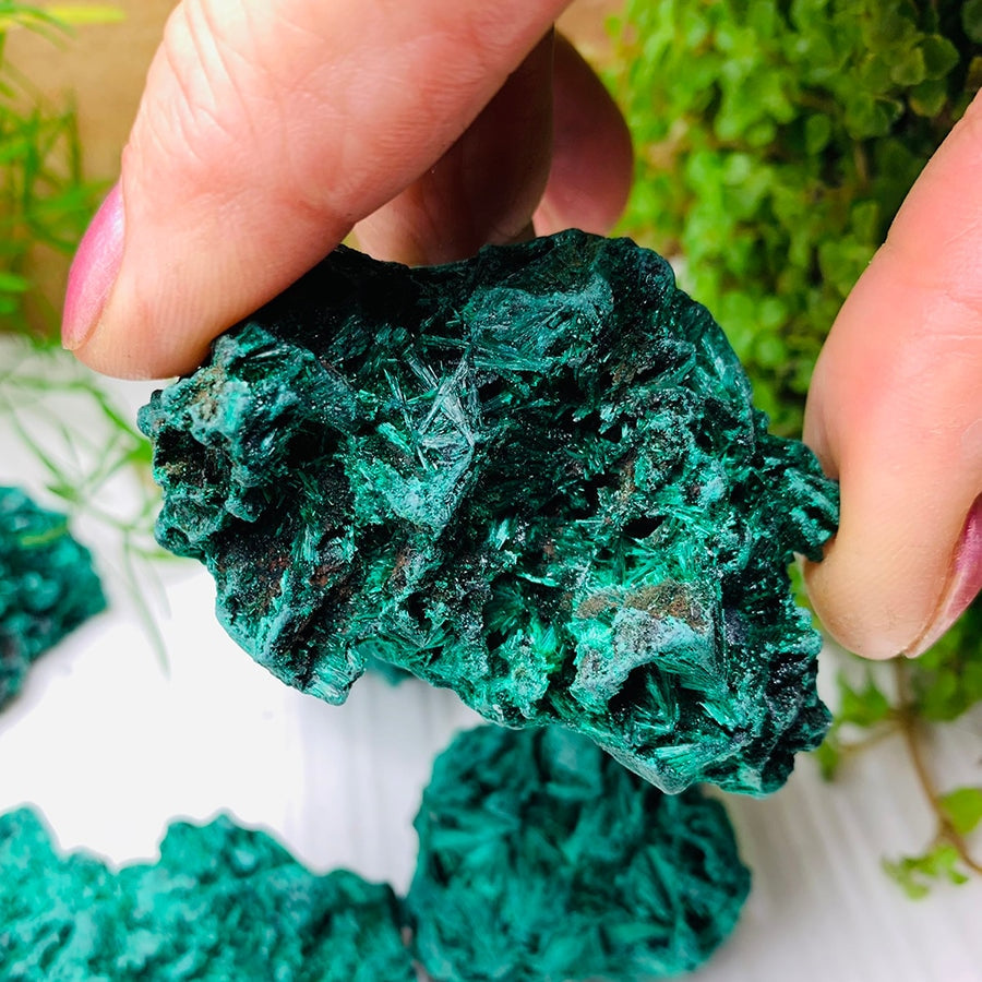 Close-up of a rough malachite piece held between fingers, its surface covered in fine glinting green crystal needles