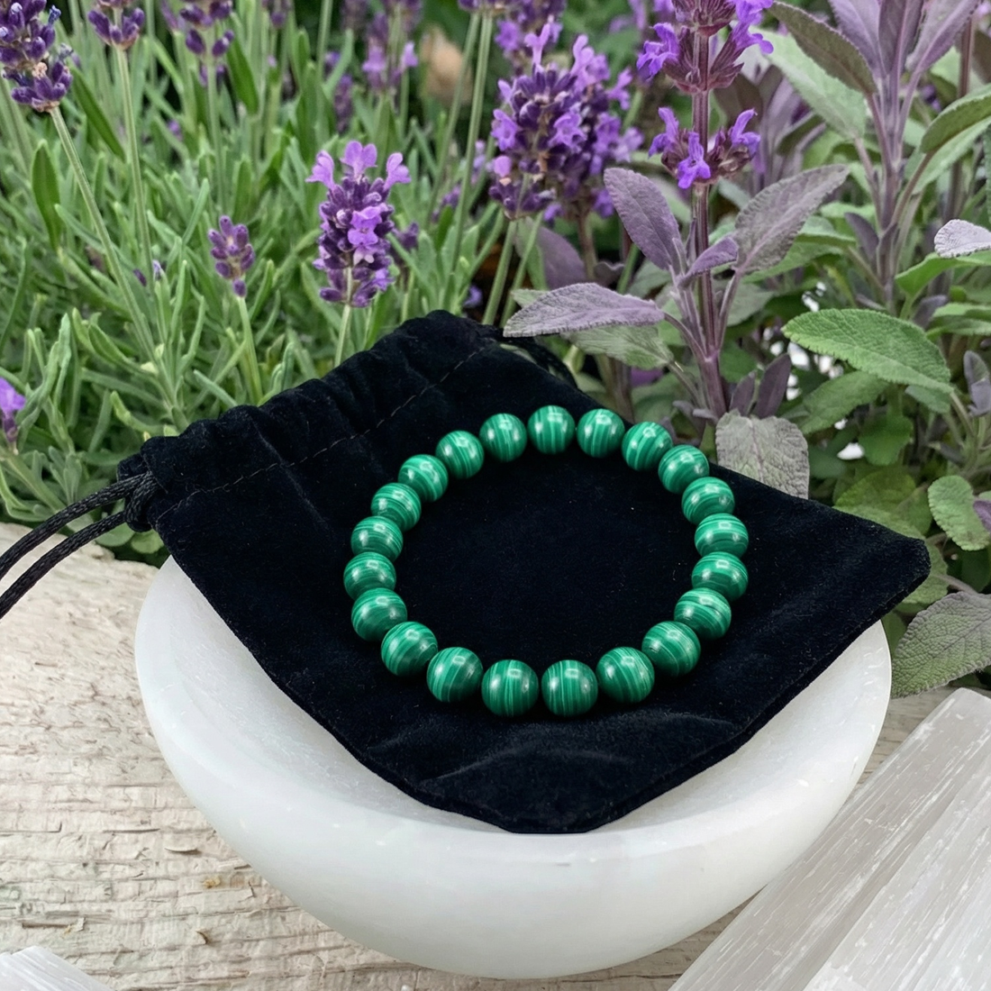 The malachite bracelet resting on its black velvet drawstring pouch in a white bowl among lavender and sage