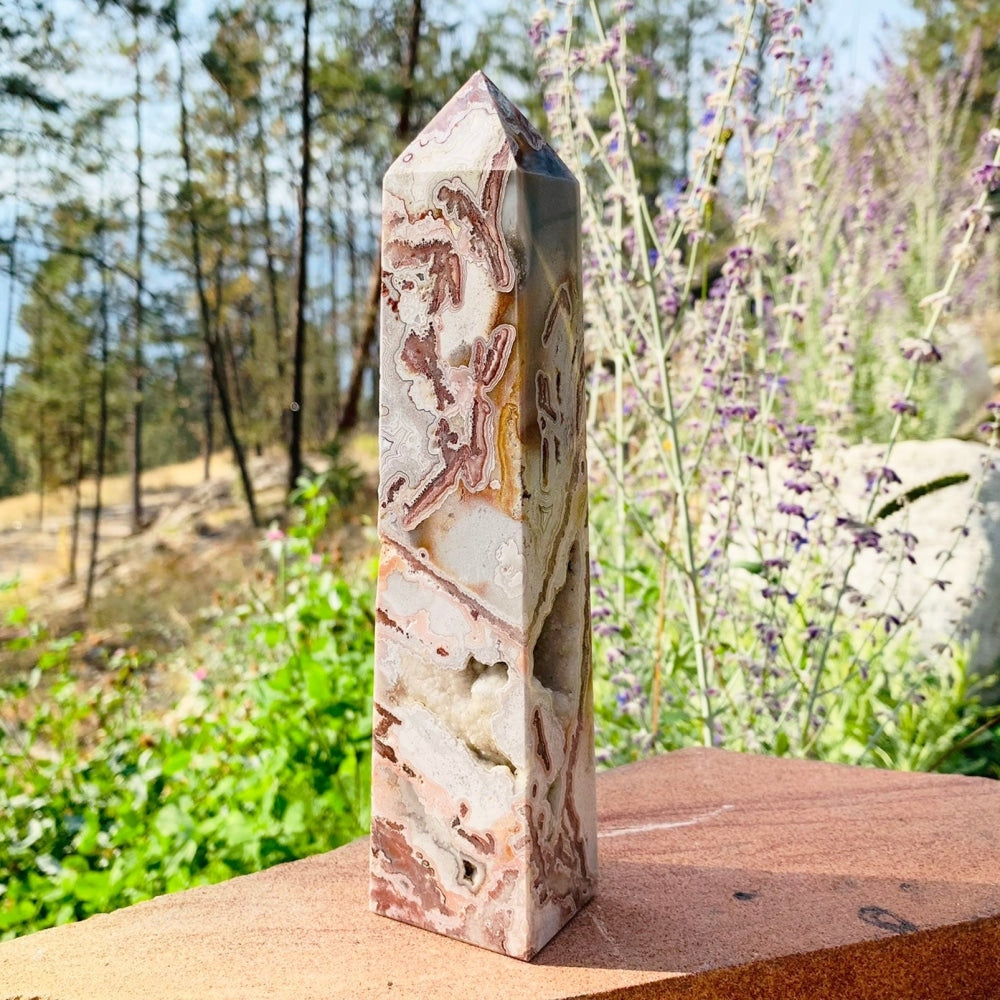 A tall Mexican lace agate druzy generator with swirling red-brown lace bands and a sparkling druzy pocket, standing outdoors