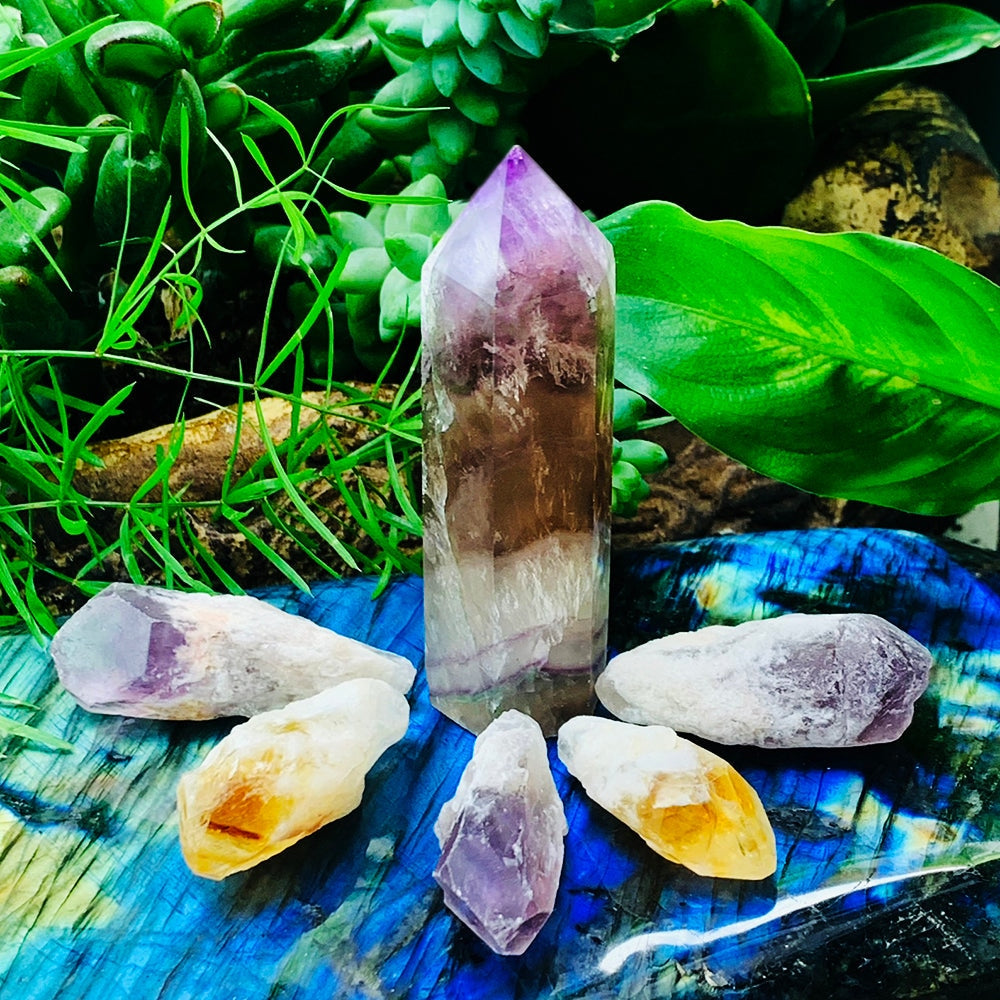 A multicolor fluorite point standing among two citrine shards and three amethyst shards on a labradorite slab