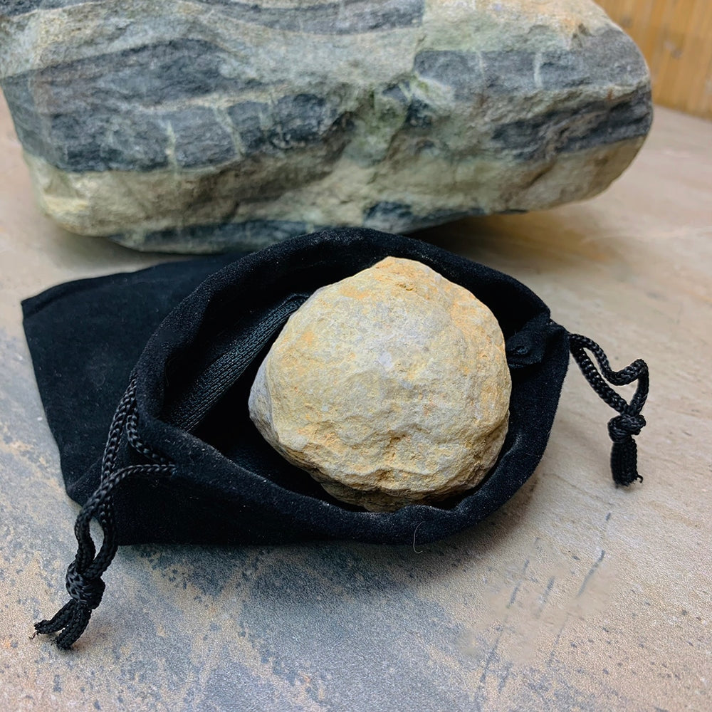 An unopened tan quartz geode resting in an open black velvet drawstring bag