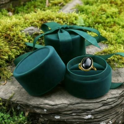 The black onyx ring nestled in an open round velvet jewelry box on a mossy stone