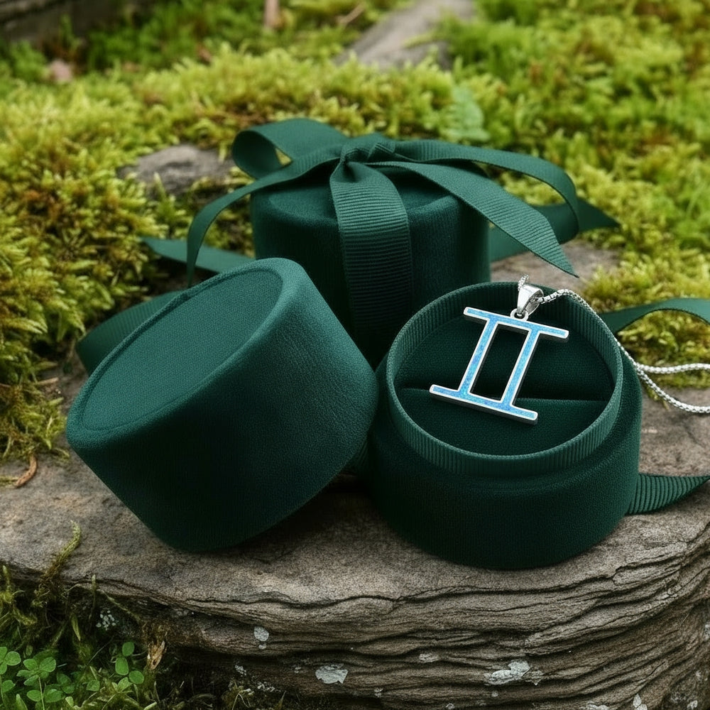 The Gemini opal pendant resting in an open round green velvet jewelry box on a mossy stone