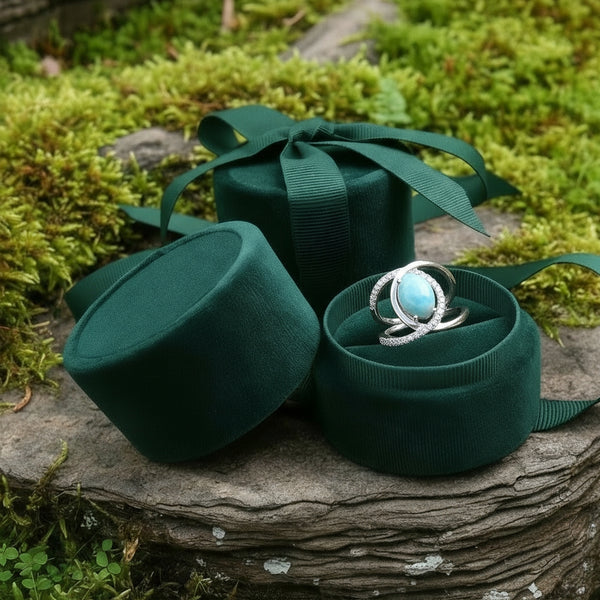 The larimar ring nestled in an open round green velvet jewelry box on mossy stone, with matching boxes and green ribbon styling the scene