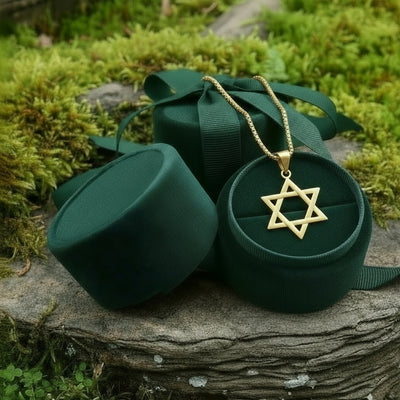 The gold Star of David pendant resting in an open round green velvet jewelry box on a mossy stone