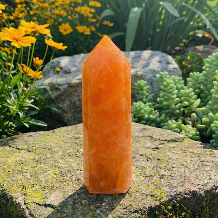 Bright orange calcite mini point standing on a stone among yellow flowers