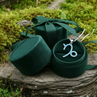 The Capricorn opal pendant resting in an open round green velvet jewelry box on a mossy stone
