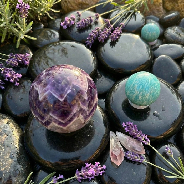 A banded dream amethyst sphere and a teal amazonite sphere on dark stones