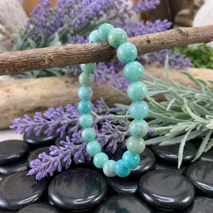 An amazonite mala bracelet of round teal beads hanging from a branch among lavender